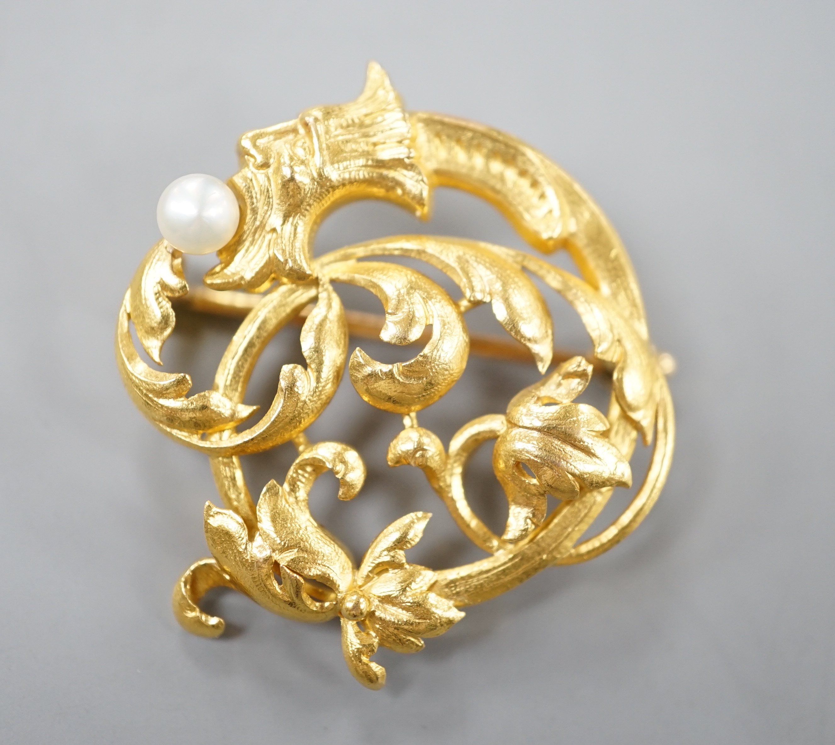 An early 20th century French yellow metal (18ct poincon mark) and cultured pearl set scrolling brooch, 30mm, gross 8.3 grams.